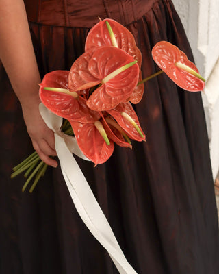 Person holding a bouquet of red flowers with a white ribbon against a dark background