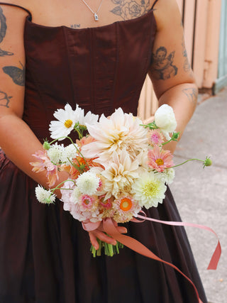 Person holding a bouquet of flowers wearing a brown dress.