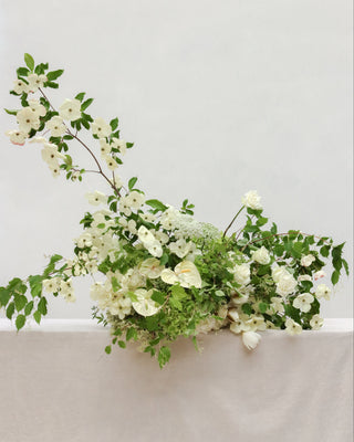 Floral arrangement with white flowers and green leaves on a light gray background