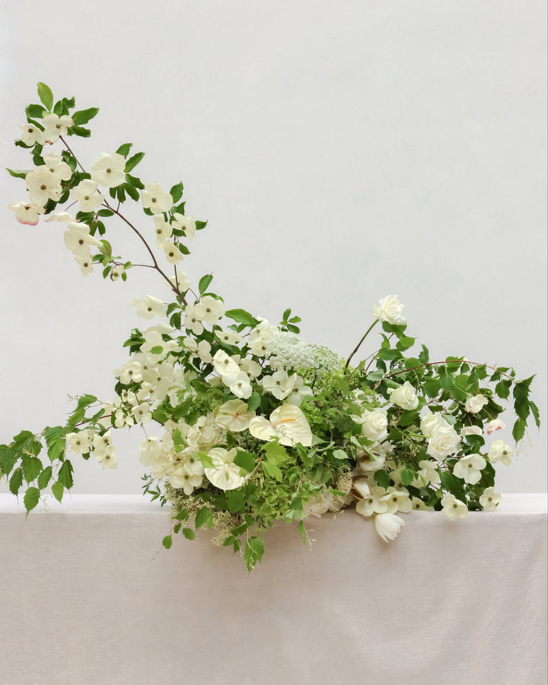 Floral arrangement with white flowers and green leaves on a light gray background