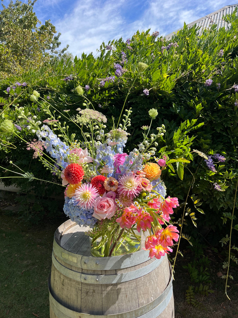 Arrangement of colorful flowers on a wooden barrel with greenery in the background