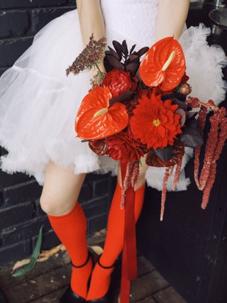 Bride wearing a white dress with red wedding bouquet and red knee-high socks.
