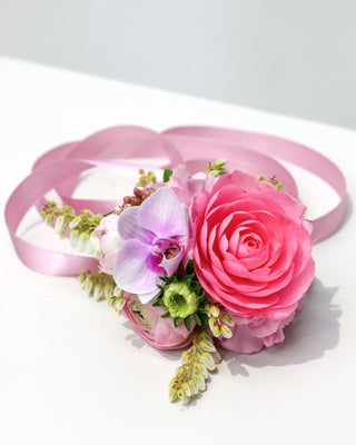 Floral arrangement wrist corsage in vibrant pink colours, finished with a soft pink satin ribbon.
