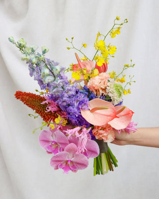 Colorful bouquet of flowers held by a person against a plain background