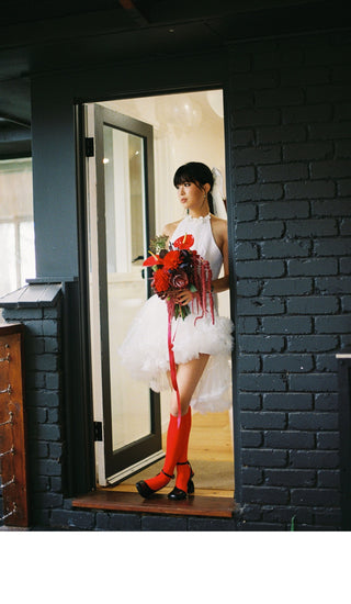 Woman in a white wedding dress holding red flowers standing in front of a black brick wall.