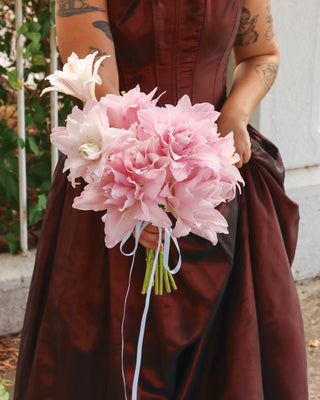 Person wearing a brown wedding dress, holding a bouquet of pink Lily flowers.