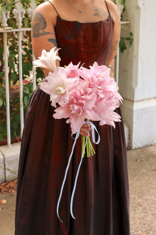 Person wearing a brown dress holding a monofloral bouquet of pink Rose Lily flowers.