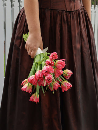 Person wearing a brown dress holding pink tulips against a white fence background