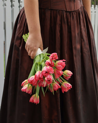 Bride wearing a brown dress holding pink tulips against a white fence background